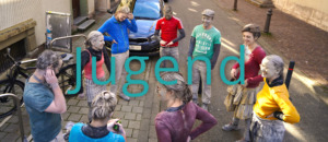 AK-Jugend Banner Bunt_Schrift3 Jugendgruppe mit Farbpuder versammelt sich im Freien.